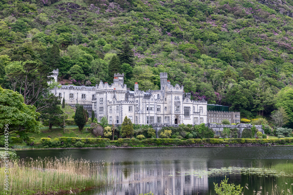Kylemore Abbey in Connemara, Ireland, reflecting on the calm waters of Pollacapall Lough. The Gothic Revival building is surrounded by lush greenery and dense woodland