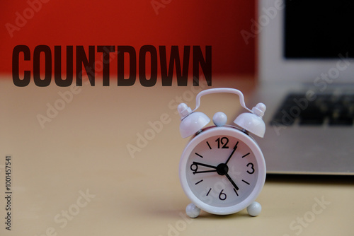 White alarm clock with text of COUNTDOWN as a time management concept with blurry laptop as background.  photo