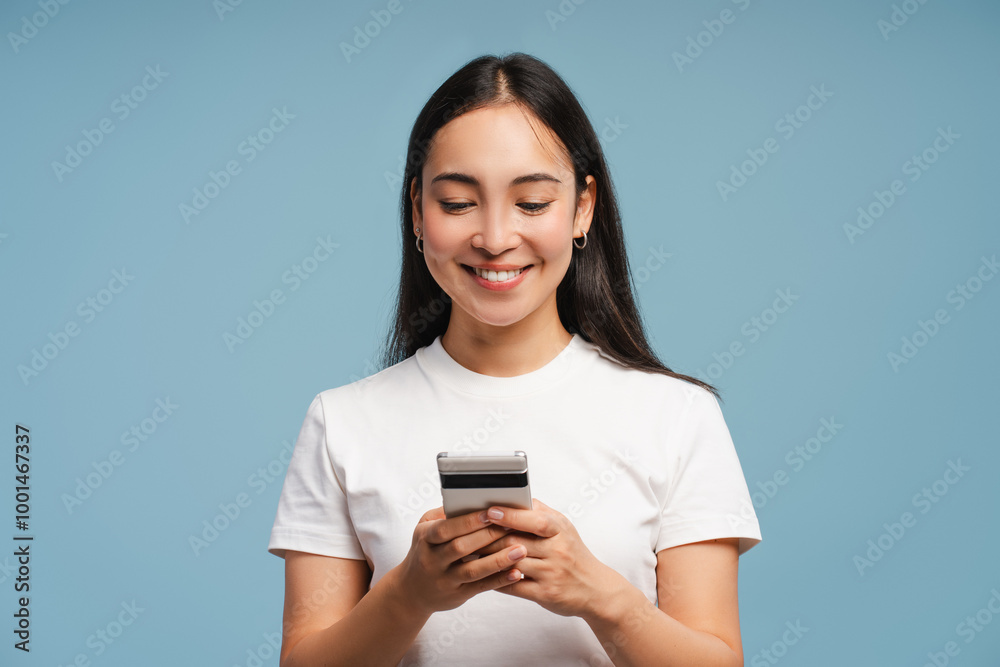 Young, smiling Asian woman using smartphone and smiling on blue background Young, smiling Asian woman using smartphone and smiling on blue background