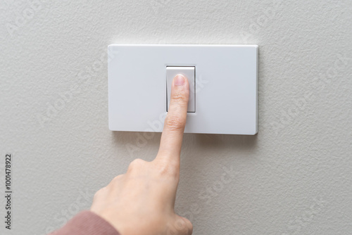 Close up of hand of woman turn off on lighting switch at home room. Finger pushing light switch turn on or off white switch on wall for saving, control power electrical energy, eco environment concept