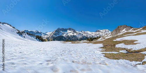 A wide-angle shot of a snowy mountain range under a clear blue sky, with patches of greenery visible on the slopes. photo