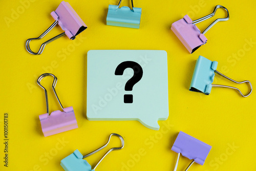 Question mark speech bubble isolated on yellow background surrounded by colorful paper clip.  photo