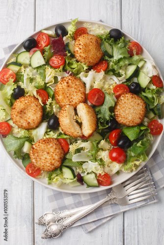 Fried goat cheese salad with tomato, olive, cucumber and lettuce closeup on the plate on the table, Vertical top view from above