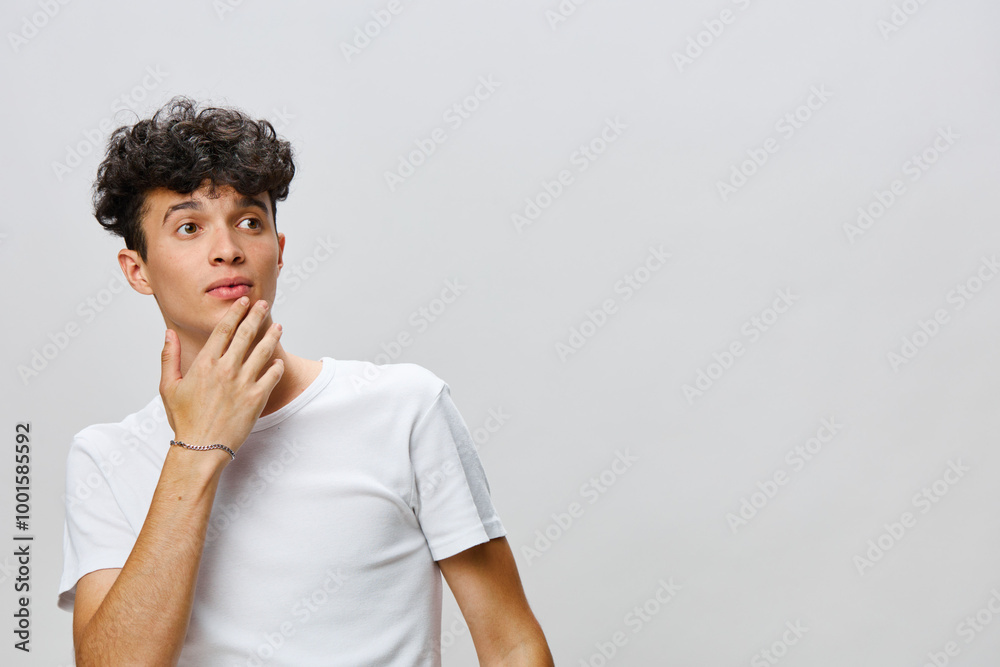 Portrait of a young man with curly hair, thoughtfully looking away against a neutral grey background Casual attire with a contemplative expression conveys a sense of curiosity and interest Portrait of a young man with curly hair, thoughtfully looking away against a neutral grey background Casual attire with a contemplative expression conveys a sense of curiosity and interest