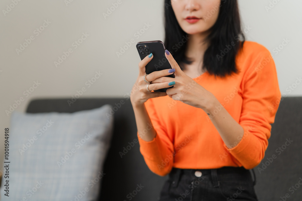 Woman Using Smartphone: A close-up shot of a young woman in an orange sweater using her smartphone, capturing the modern-day reliance on technology for communication and entertainment. Woman Using Smartphone: A close-up shot of a young woman in an orange sweater using her smartphone, capturing the modern-day reliance on technology for communication and entertainment.