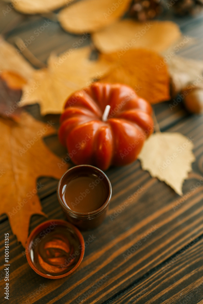 Top view of a paintbrush placed on dried autumn leaves with acorns, pine cones, and a pumpkin on a rustic wooden background