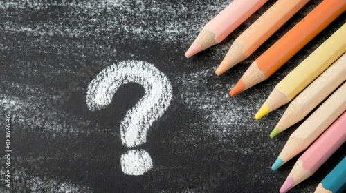 Three colored pencils beside a chalk question mark on a dark surface during d...