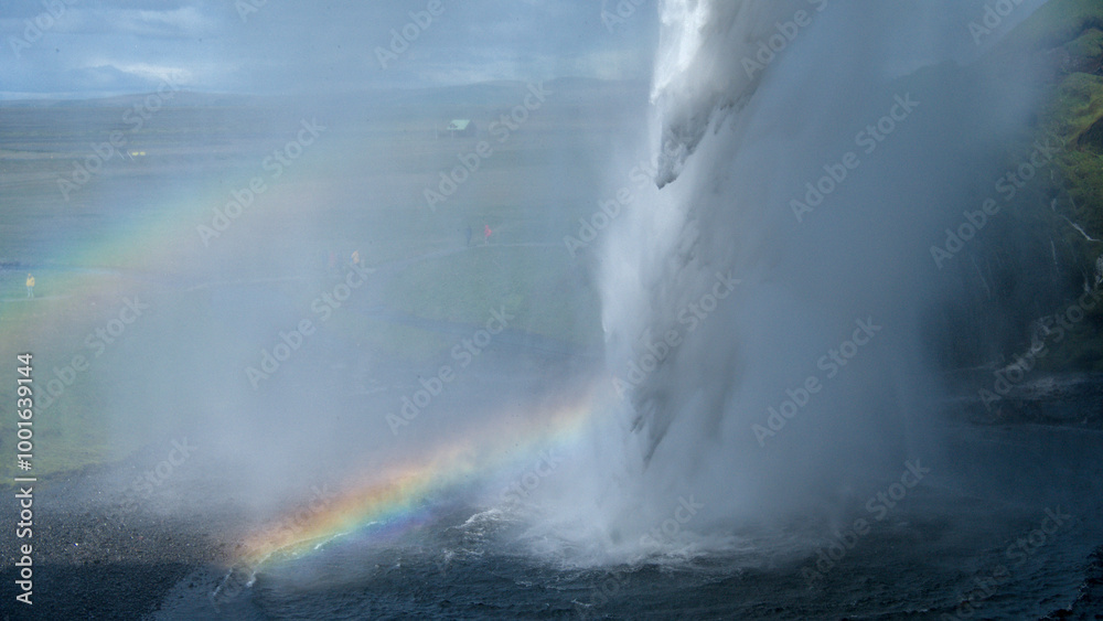 The waterfall of Seljalandsfoss in Iceland from behind the water with a rainbow The waterfall of Seljalandsfoss in Iceland from behind the water with a rainbow