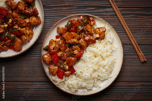 Two plates with steaming Chinese kung pao chicken with rice, veggies, and peanuts in spicy sauce. Top view on wooden background. Perfect for lunch or dinner photo