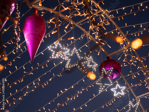 Obraz na płótnie Closeup of Christmas and New Year holidays multicolored decorations and glowing string fairy lights hanging above the road at night outdoors. Winter holidays celebration concept. w salonie