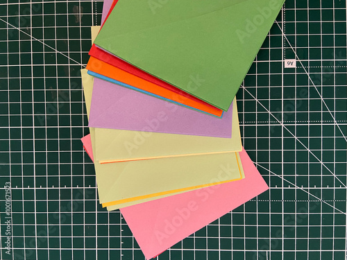 Close-up of colored paper envelopes laid out on a marked green surface.