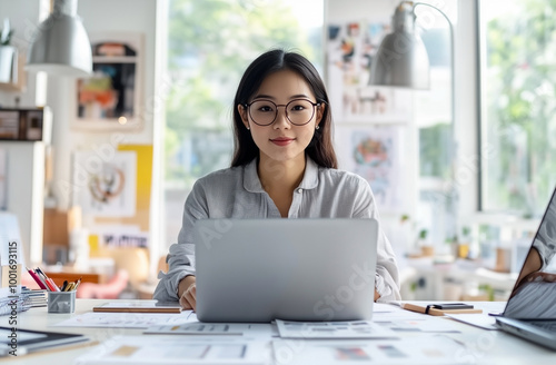 A professional photo of a female sitting at her desk in front of a laptop, wearing a shirt.