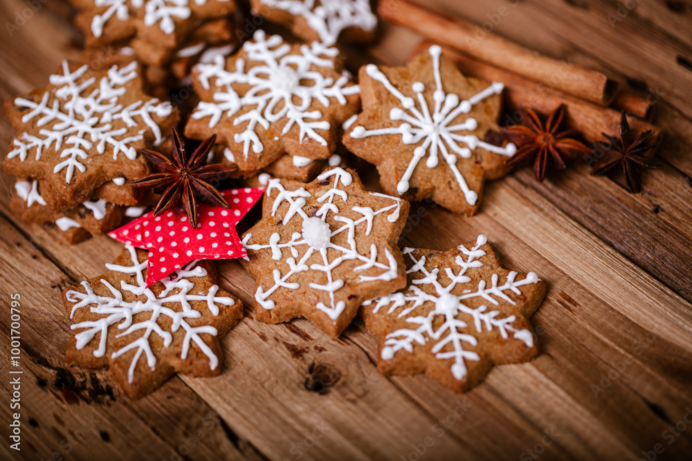 Gingerbread cookies with white snowflake icing, arranged with star anise, cinnamon sticks, and a red fabric star on a rustic wooden surface, creating a festive holiday atmosphere. . Gingerbread cookies with white snowflake icing, arranged with star anise, cinnamon sticks, and a red fabric star on a rustic wooden surface, creating a festive holiday atmosphere. .