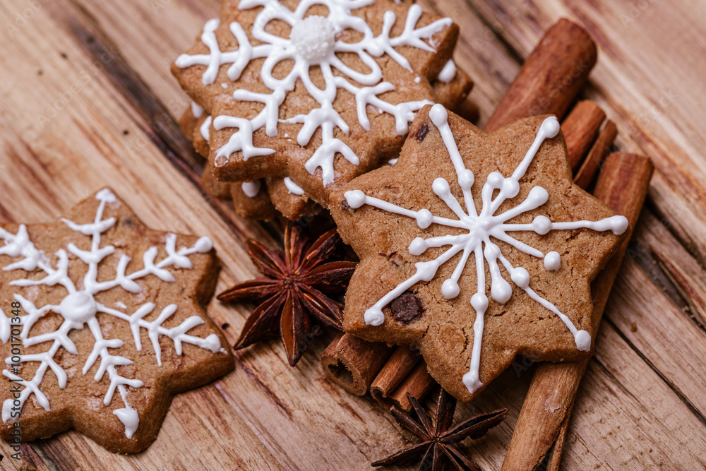 Gingerbread cookies with white snowflake icing on top of cinnamon sticks and star anise, placed on a rustic wooden background, creating a festive and warm holiday atmosphere.