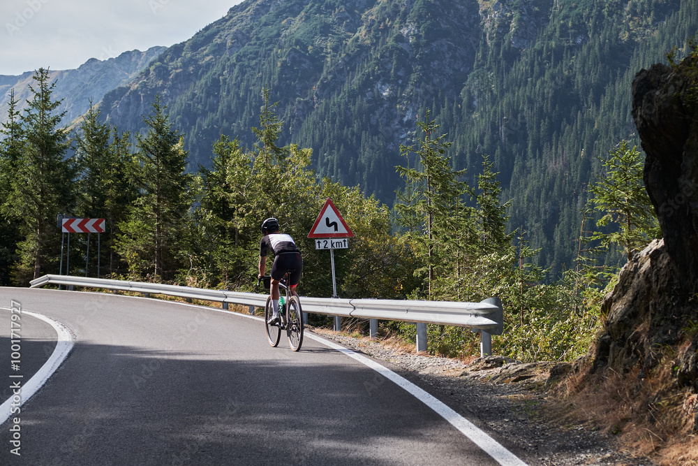 Man cyclist riding a winding mountain road with a sign warning of a bend ahead. Sport motivation. Adventure travel on bike.Mountain background.Cycling in Carpathian Mountains. Transfăgărășan. Romania Man cyclist riding a winding mountain road with a sign warning of a bend ahead. Sport motivation. Adventure travel on bike.Mountain background.Cycling in Carpathian Mountains. Transfăgărășan. Romania