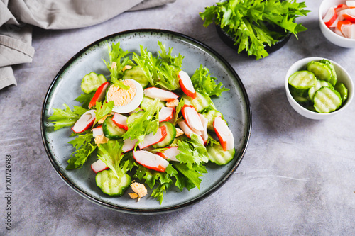 Appetizing salad of crab sticks, cucumber, leaves and egg on a plate on the table