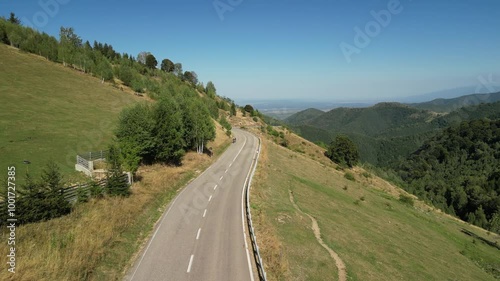 Aerial view of a winding road in a mountain landscape. A car and two cyclists drive along a curvy asphalt road.Active adventures and the concept of travel by bike.Gravel bike riding in nature.