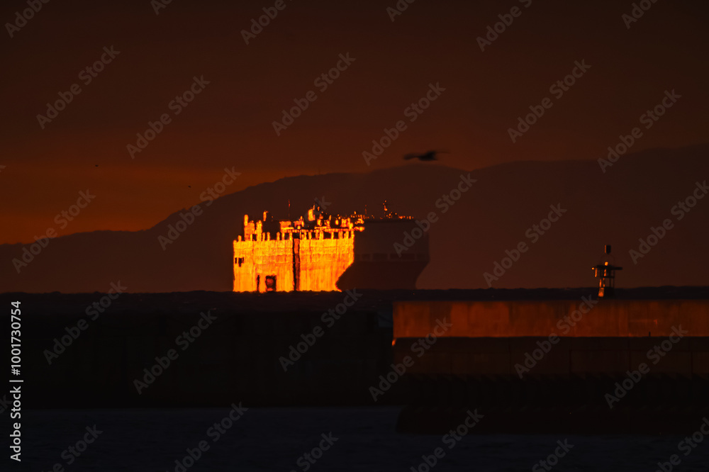 Obraz premium 昇る朝日を浴びて輝きながら港に迫る船影20240914