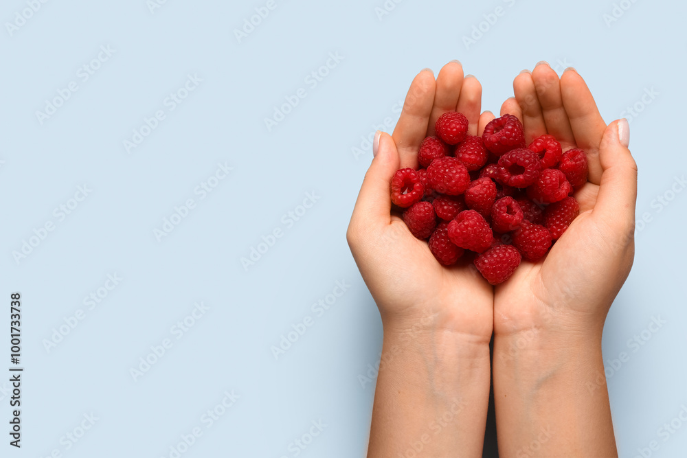 Woman holding fresh raspberries on blue background
