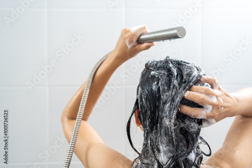 Young woman in shower rinse shampoo foaming with water dripping on hair and body. Taking shower relaxing under warm running water. Female washing her hair and hand to massage head while washing hair.