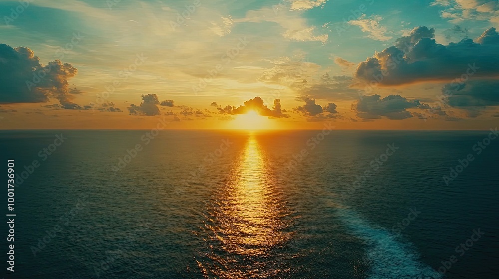 Obraz premium A vibrant sunset over a calm ocean with a golden glow and a trail of light reflecting on the water.