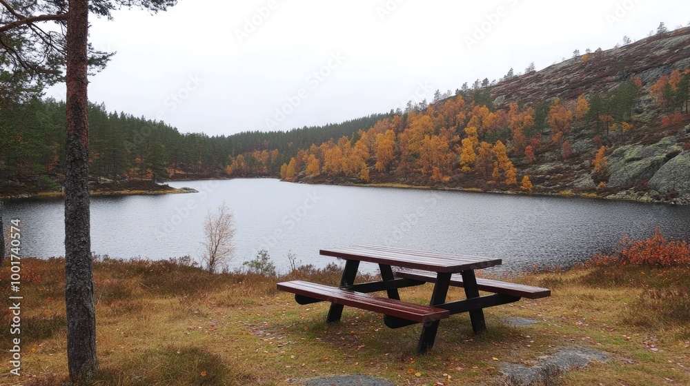 A wooden picnic table sits overlooking a lake with fall foliage on the hillside.