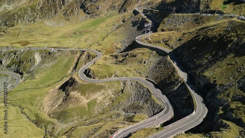 Aerial view of a winding mountain road with cars driving on it. The road is surrounded by green grass and rocky hills. Perfect for travel, adventure, or nature themes. Transfagarasan in Romania.