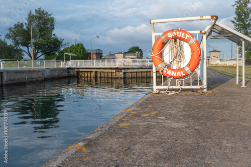 Billede på lærred Orange Life Ring Hanging on the Waters Edge at the Sault Ste Marie Canal with a