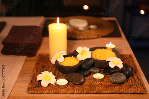 Spa composition with plumeria flowers and burning candles on table in dark salon, closeup