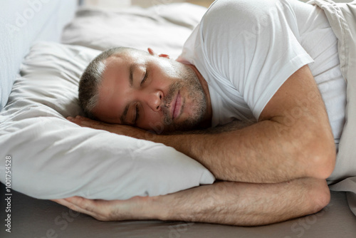 European middle aged well-slept man lying in bed with closed eyes, resting in bedroom on the side in bedroom, having nap