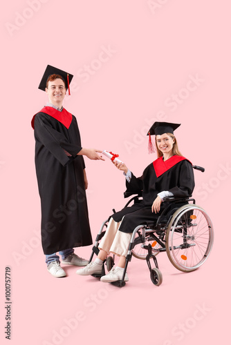 Female graduate in wheelchair receiving diploma on pink background