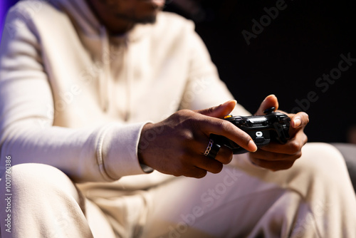 Close up shot of gamepad held by man playing entertaining videogame in rgb lit apartment. Focus on joystick used by person in blurry background to enjoy gaming on console system