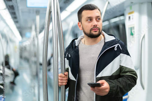 Interested young man browsing messages on his phone on way to work in modern metro car.. photo