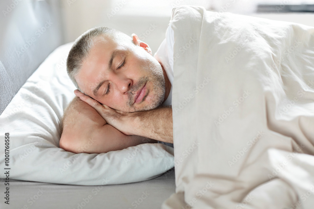 European middle aged man resting head on hands, sleeping in comfortable bed, napping in his bedroom at home European middle aged man resting head on hands, sleeping in comfortable bed, napping in his bedroom at home