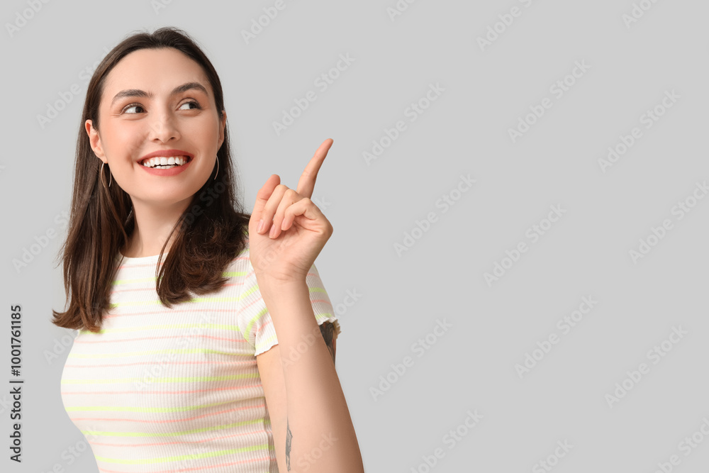Smiling young woman pointing at something on grey background Smiling young woman pointing at something on grey background