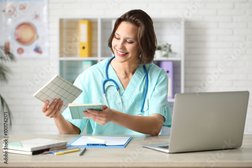 Beautiful female doctor with notebooks and modern laptop at table in clinic