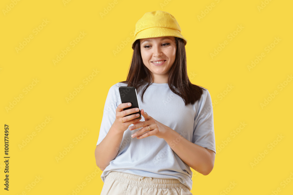 Young woman using mobile phone on yellow background