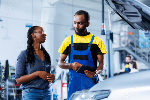 Mechanic at auto repair shop conducts annual vehicle checkup, informing customer about needed brakes replacement. African american garage worker talks with customer after finishing car inspection