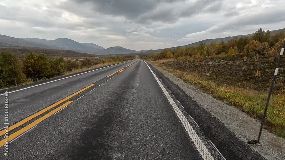 Long straight road leads through autumn landscape with mountains in the background and cloudy sky, bicycle tour, Dovrefjell, National Park, Norway, Europe Long straight road leads through autumn landscape with mountains in the background and cloudy sky, bicycle tour, Dovrefjell, National Park, Norway, Europe