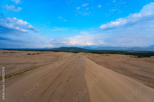 Expansive desert dunes under a dramatic sky with distant mountains