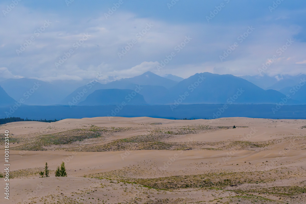 Expansive desert dunes under a dramatic sky with distant mountains Expansive desert dunes under a dramatic sky with distant mountains