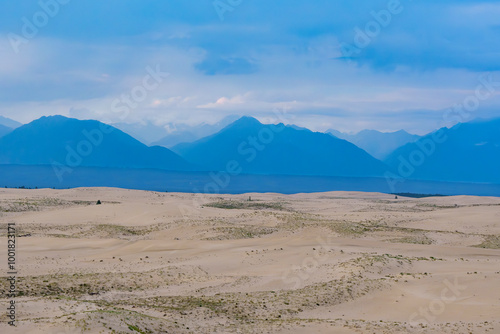 Expansive desert dunes under a dramatic sky with distant mountains