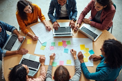 A diverse team engages in a brainstorming session around a table filled with laptops, sticky notes, and papers, representing collaboration, creativity, and planning in a modern workspace. photo