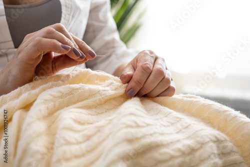 Clothes repair concept. A woman uses her hands to sew up a hole in a beige knitted garment