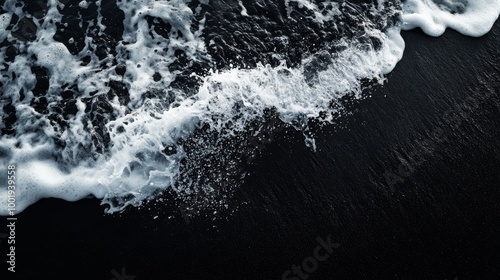 A close-up shot of a wave breaking on a black sand beach, with the dark sand contrasting sharply with the white foam of the wave photo