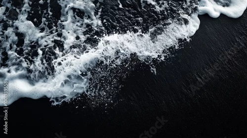 Fototapeta samoprzylepna A close-up shot of a wave breaking on a black sand beach, with the dark sand contrasting sharply with the white foam of the wave