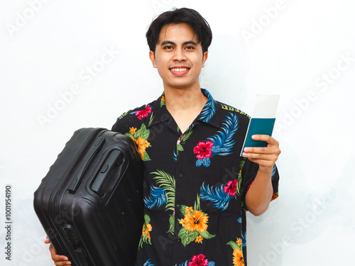 Cheerful young Asian man in summer casual attire holding a passport and suitcase, ready for a trip. Isolated on a white background, perfect for travel-themed content. photo