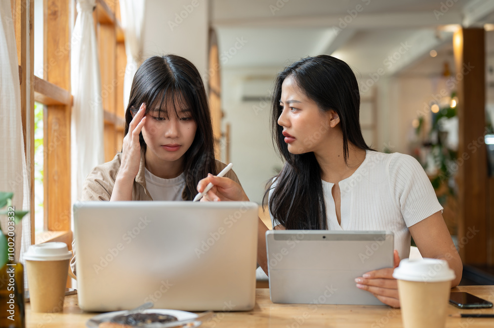 Two serious and stressed Asian female friends are working remotely together from a coffee shop. Two serious and stressed Asian female friends are working remotely together from a coffee shop.