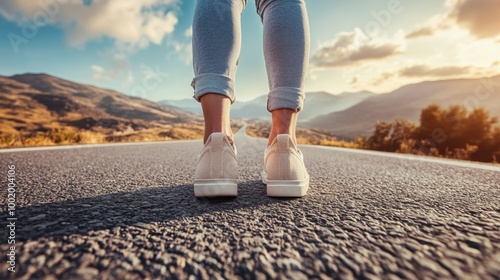Person standing on an open road wearing light-colored sneakers against a scenic landscape with a long stretch ahead