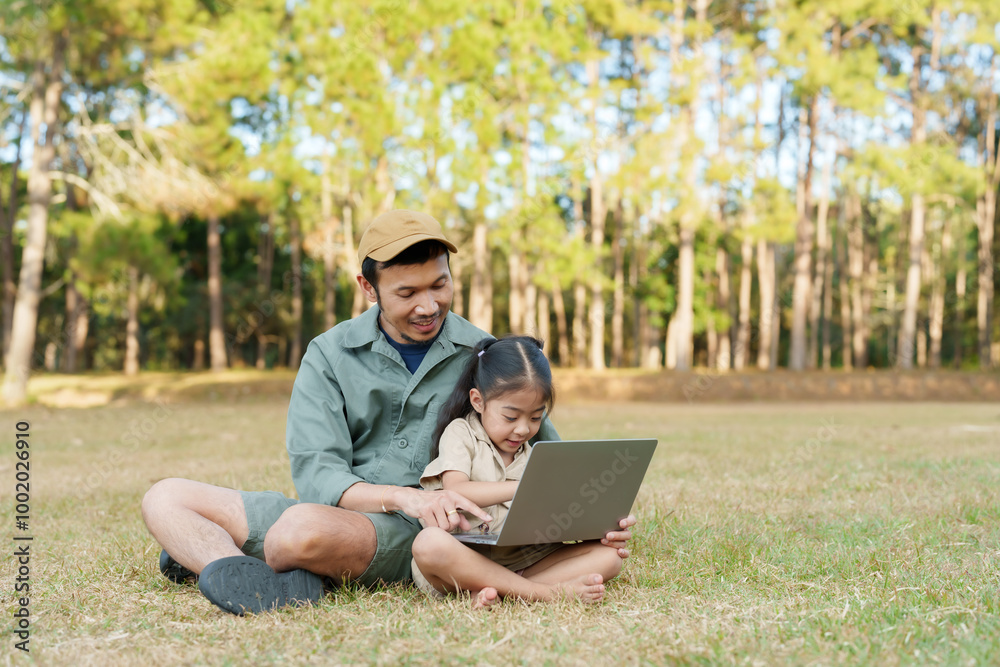 Father and daughter sitting together on grass in national park, using laptop. Father teaching daughter in peaceful outdoor setting, surrounded by trees and enjoying nature together. Father and daughter sitting together on grass in national park, using laptop. Father teaching daughter in peaceful outdoor setting, surrounded by trees and enjoying nature together.